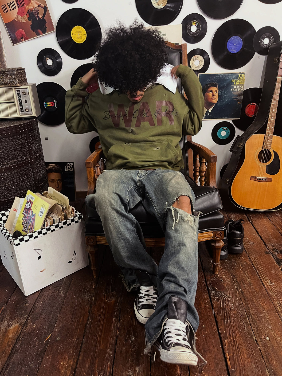 Warfare Hoodie worn with distressed jeans, seated